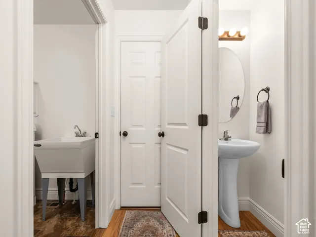 Pedestal sink with chrome faucet, oval mirror, and wood-finish flooring