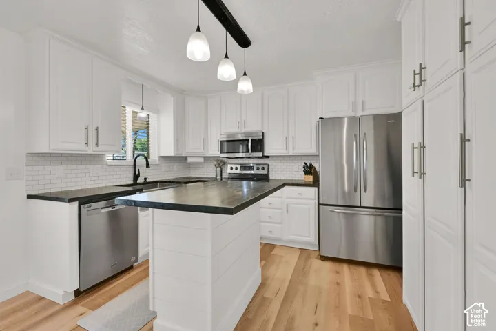 Kitchen featuring white cabinetry, a central island, stainless steel appliances, dark countertops, and wood-finish flooring