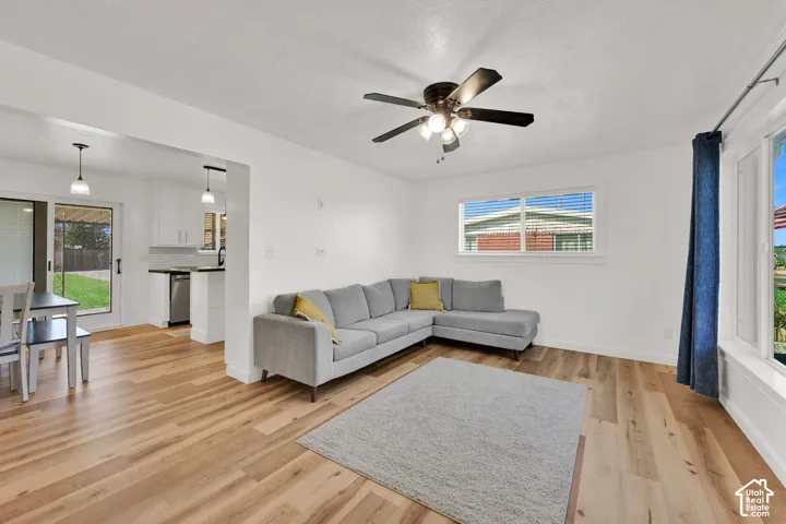 Spacious living area featuring wood-finish flooring, a ceiling fan with integrated lighting, and multiple windows