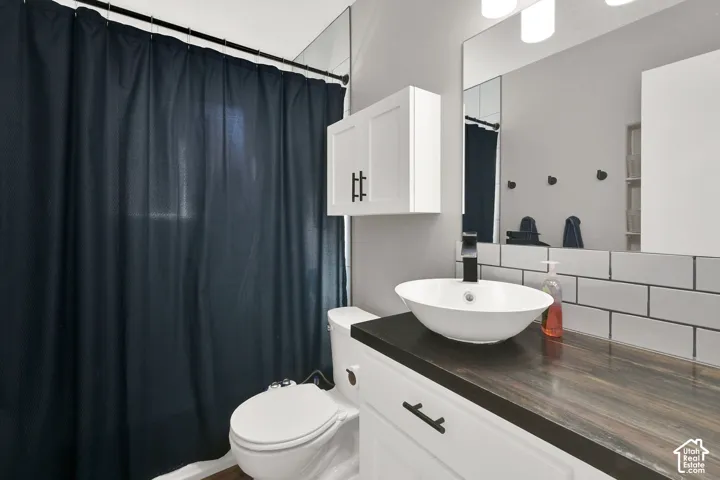 Wood-finish countertop with a vessel sink, white subway tile backsplash, and a large wall-mounted mirror