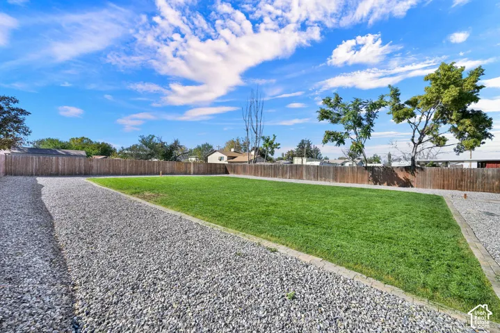 Spacious yard featuring a large grassy area, gravel pathways, a wood privacy fence, and mature trees