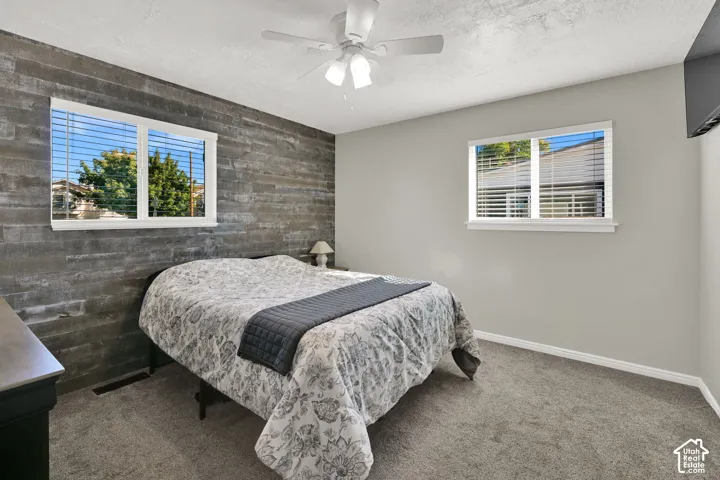 Accent wall with a horizontal wood-finish pattern, two windows with blinds, light gray wall paint, and gray carpet flooring