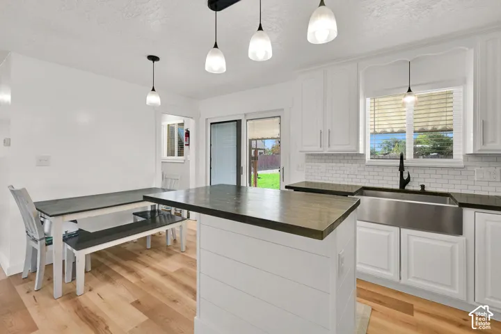 White shaker cabinetry, wood-finish flooring, white subway tile backsplash, farmhouse-style sink, and matte black fixtures