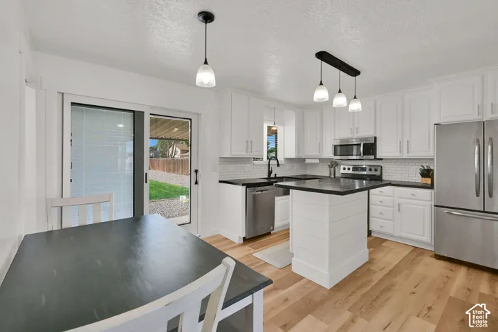 White cabinetry kitchen featuring a center island, stainless steel appliances, dark countertops, and light wood-finish flooring