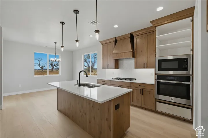 Kitchen featuring a central island with a dual-basin sink, wood-finish cabinetry, built-in stainless steel appliances, and light-toned flooring