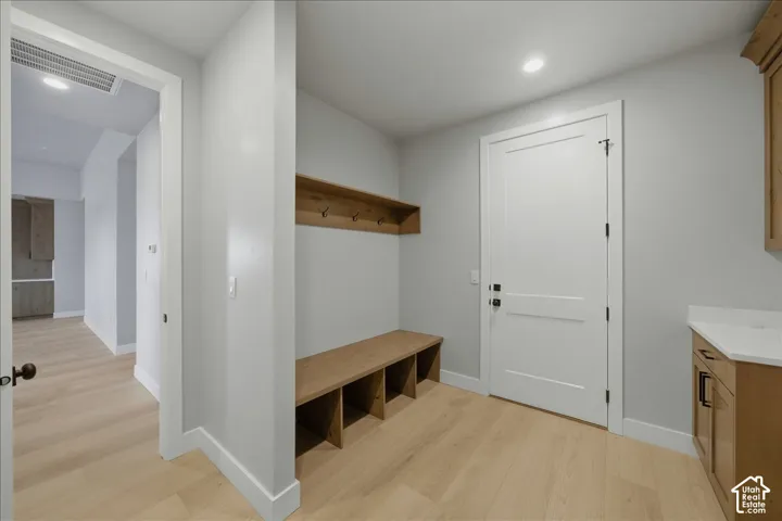 Light wood-finish flooring, built-in wooden bench with open storage, wall-mounted wood shelf with hooks, light gray walls, and white paneled doors