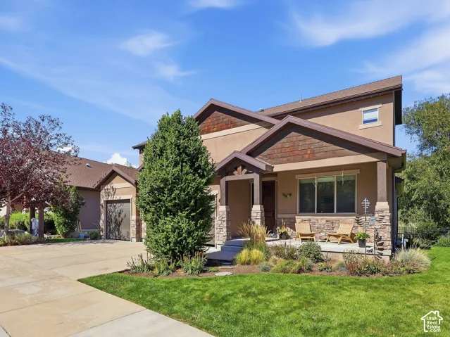 Exterior featuring a prominent front porch, stone and stucco facade, wood-shingle gables, a two-car garage, and established landscaping