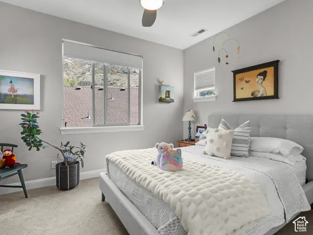 Plush carpet flooring, neutral painted walls, ceiling fan, and multiple windows providing natural light