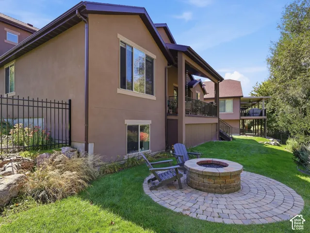 Paved patio featuring a built-in stone fire pit, surrounded by a grassy yard and mature trees