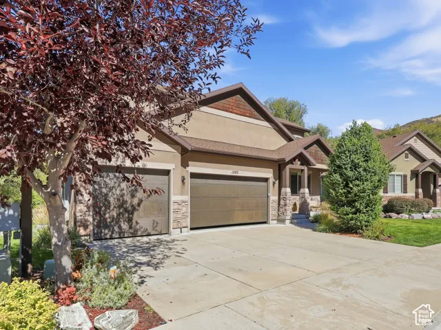 Stucco and stone facade with a multi-car driveway, two garage doors, and mature landscaping