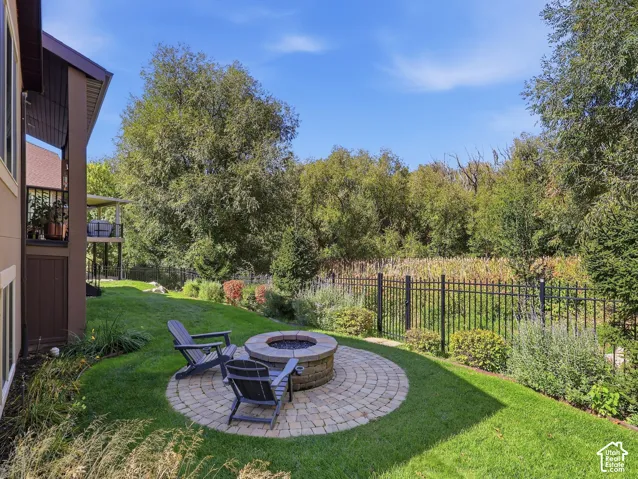 Landscaped yard featuring a circular paver patio with a built-in fire pit, surrounded by lush green lawn and mature plantings