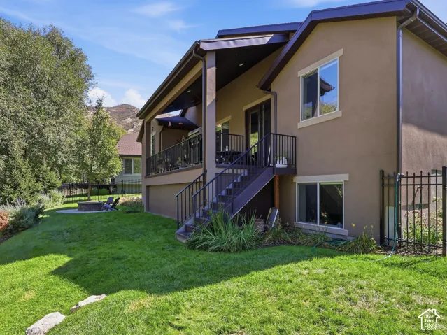 Spacious backyard featuring a manicured lawn, paved patio with fire pit, and mature trees