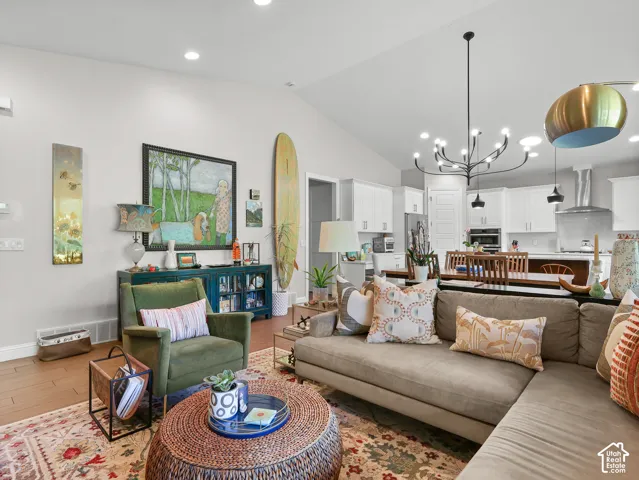 Vaulted ceiling with a contemporary chandelier, wood-finish flooring, and white shaker-style cabinetry with stainless steel appliances