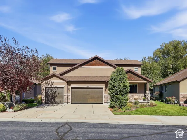 Stucco exterior featuring stone accents, a covered front porch, and an attached two-car garage with an additional single-car garage