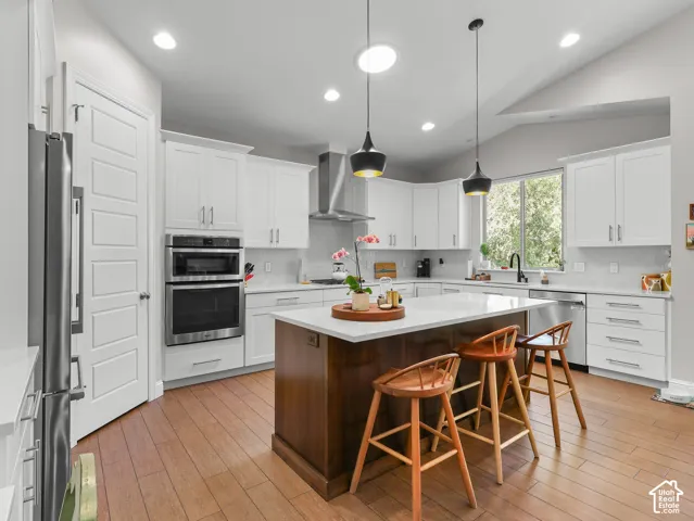 Kitchen featuring white shaker cabinetry, stainless steel appliances, wood-finish flooring, a center island with countertop seating, and recessed lighting