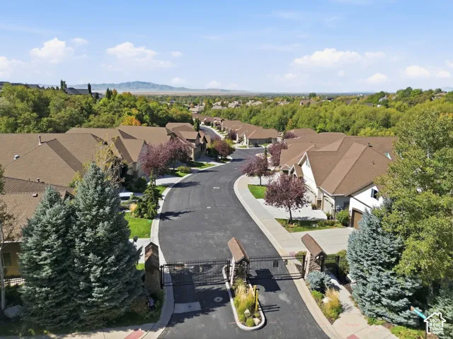 Gated community entrance with mature landscaping and paved roadways, surrounded by abundant greenery and distant mountains