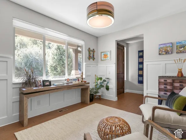 Room featuring wood-finish flooring, wainscoting, an expansive window, and a built-in light fixture