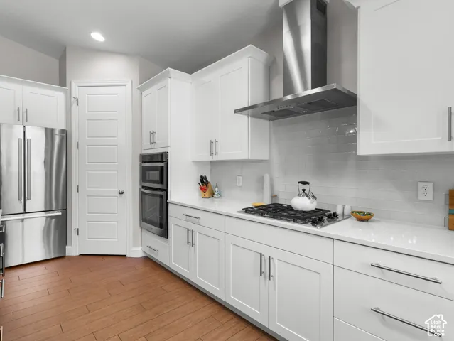 Modern kitchen featuring white shaker cabinetry, stainless steel appliances, a gas range with range hood, and wood-finish flooring