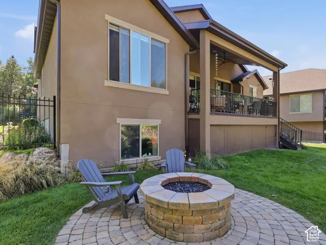 Exterior stucco finish with a covered upper-level deck, a lower-level patio with paver stones, a built-in stone fire pit, and an iron fence