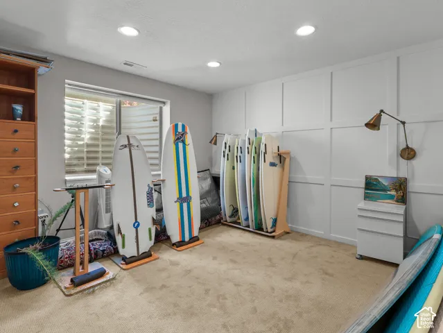 Recessed ceiling lighting, paneled accent wall, wood-finish built-in shelving, carpet flooring, and a window with blinds
