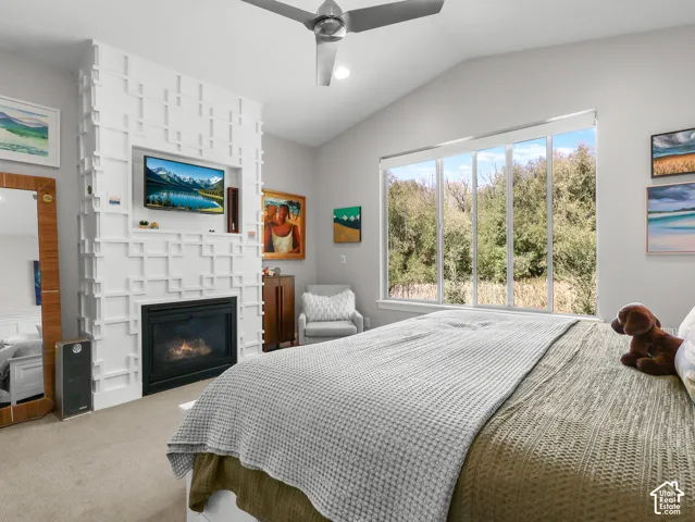 Vaulted ceilings with a ceiling fan, a contemporary fireplace with a decorative surround, large windows, and carpet flooring