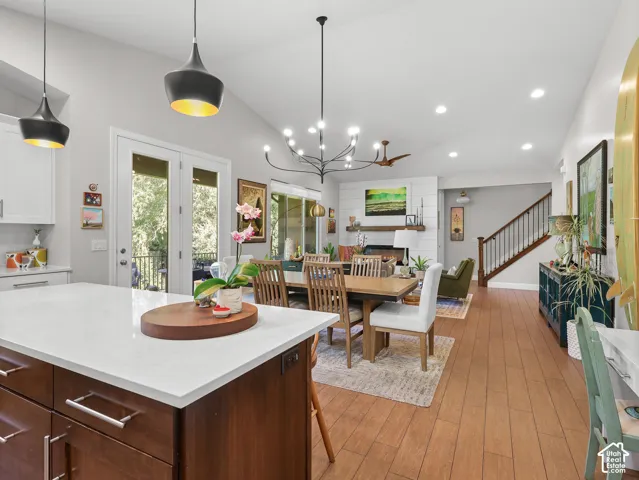 Open-concept kitchen and dining area featuring a wood-finish island with white quartz countertop, stainless steel appliances, pendant lighting, hardwood flooring throughout, and abundant natural light from glass doors opening to outdoor space