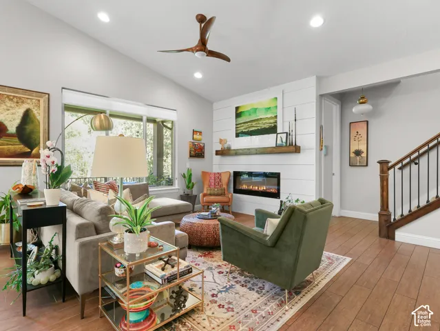 Vaulted ceilings with recessed lighting, wood-finish flooring, linear electric fireplace with wood mantel, built-in shiplap wall feature, and a staircase with wood newel posts and wrought iron balusters