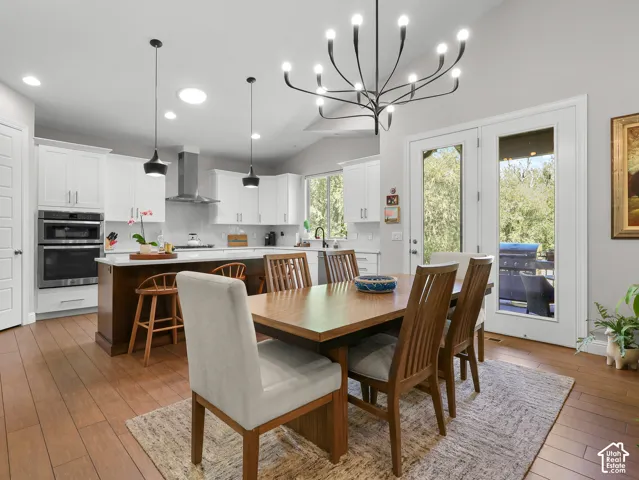 Open-concept kitchen and dining area featuring wood-finish flooring, white cabinetry, a center island with seating, a stainless steel double oven, and pendant lighting