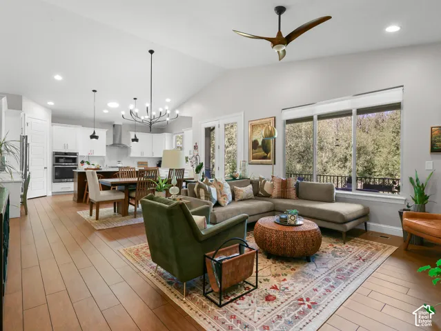Vaulted ceiling, recessed lighting, wood-finish flooring, white cabinetry, and a black chandelier