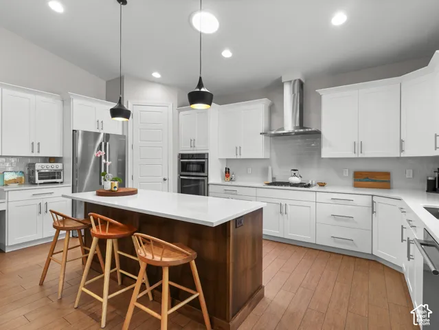 Kitchen featuring wood-finish flooring, white cabinetry, a large central island with a white countertop, stainless steel appliances, and recessed lighting