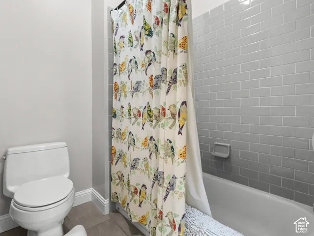 White toilet with a dual-flush mechanism, subway tile bath surround, and a built-in shower niche