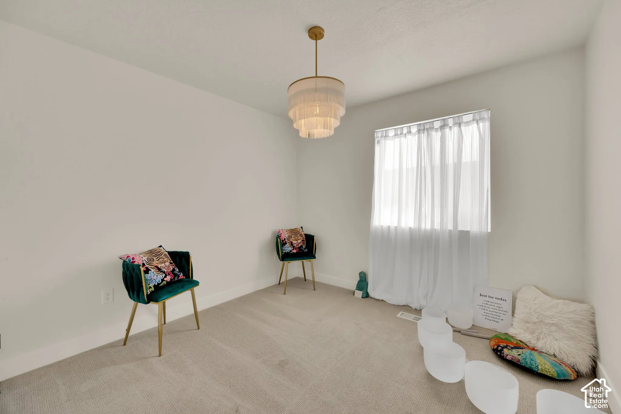 Neutral wall paint, carpeted flooring, a tiered chandelier, and a window with sheer curtains