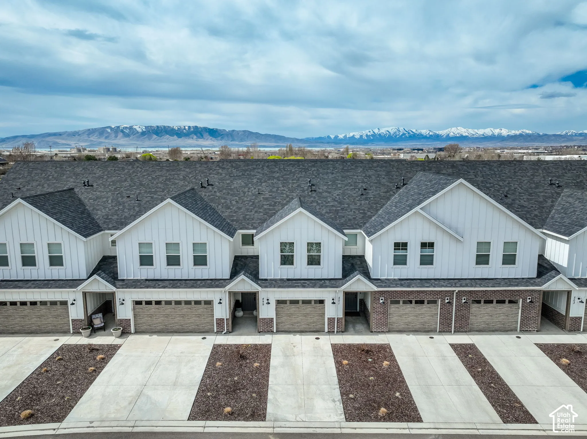 Contemporary townhome exteriors featuring white vertical siding, dark shingle roofing, and integrated garages with textured doors