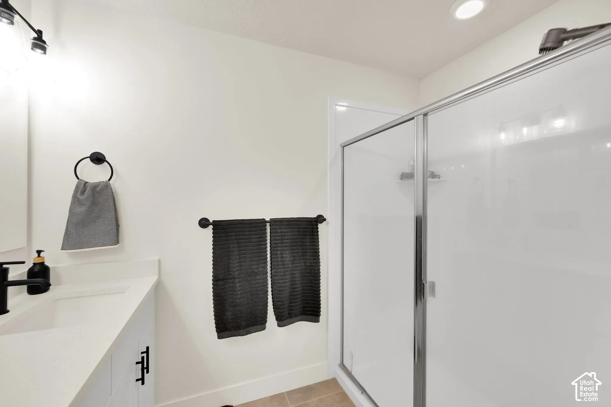 Shower enclosure with sliding glass door, white vanity with integrated sink, matte black faucet, and track lighting