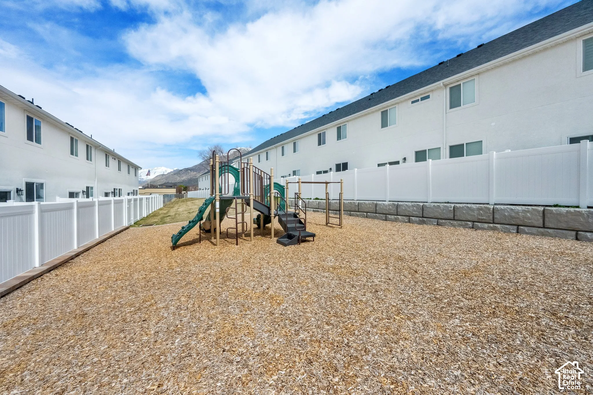 Community playground featuring multi-level play structures, wood chip surfacing, and white vinyl fencing