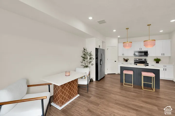 Wood-finish flooring throughout, white cabinetry with dark hardware, stainless steel appliances, central kitchen island with seating, and recessed lighting