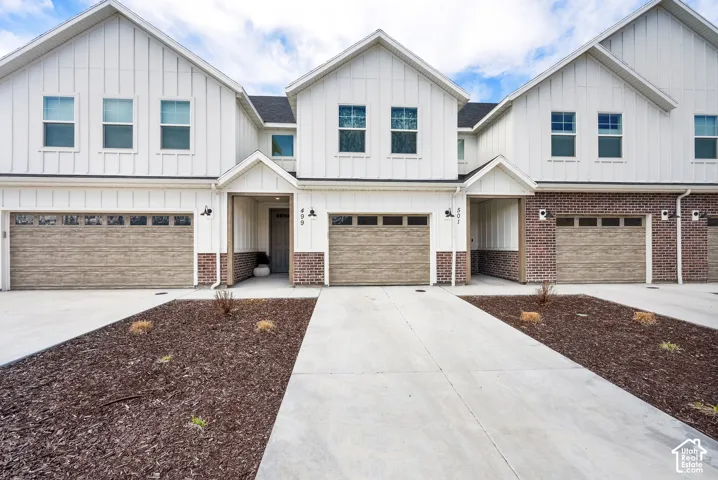 Modern farmhouse exterior with vertical white siding, brick accents, wood-finish garage doors, concrete driveways, and front entry porch