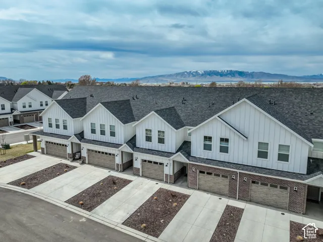 Modern farmhouse-style townhomes featuring white vertical siding, dark shingle roofing, and brick accents