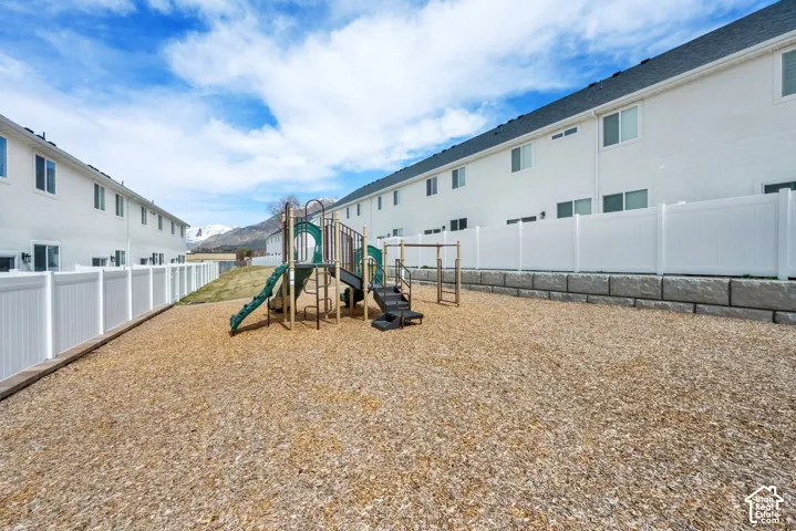Community playground featuring multi-level play structures, wood chip surfacing, and white vinyl fencing