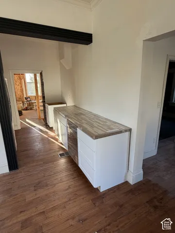 Wood-finish flooring with a side counter featuring white cabinetry and a butcher block style countertop