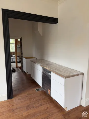 Wood-finish flooring, white cabinetry, integrated appliance, wood-look countertop, and custom-trimmed doorway