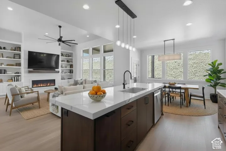 Open-concept living space featuring a central kitchen island with a sink, stainless steel appliances, and sleek pendant lighting