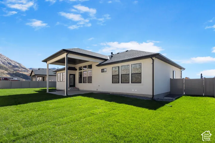 Expansive green lawn with a covered patio, multiple large windows, and a privacy fence
