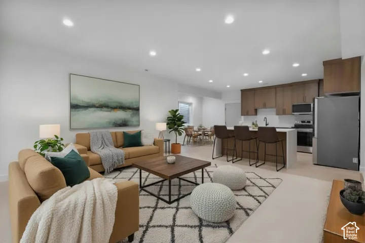 Open-concept living space featuring recessed lighting, a kitchen island with seating, wood-finish cabinetry, stainless steel appliances, and light-toned flooring
