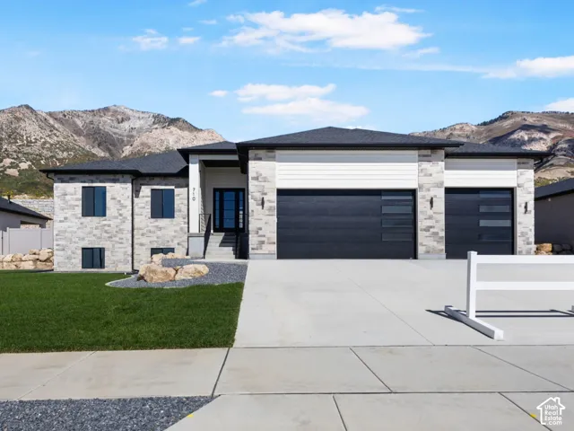 Contemporary exterior with stone and siding accents, dual garage doors, a concrete driveway, and a manicured lawn