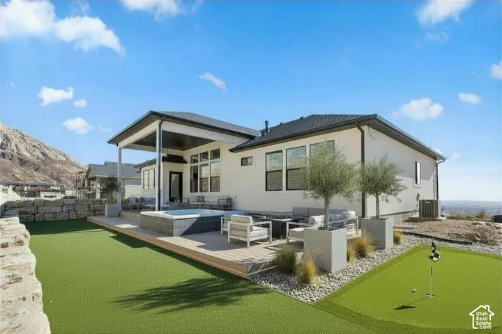 Expansive outdoor space featuring a putting green, covered patio, outdoor spa, and a stone retaining wall