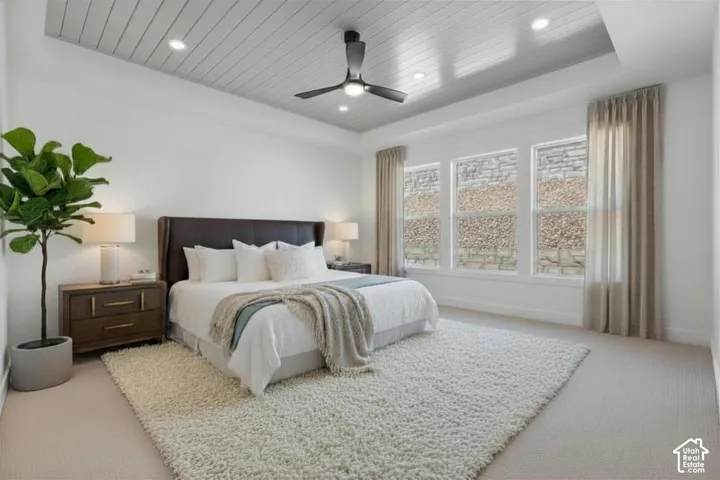 Recessed ceiling with plank detailing, modern ceiling fan, three expansive windows, and plush carpeting