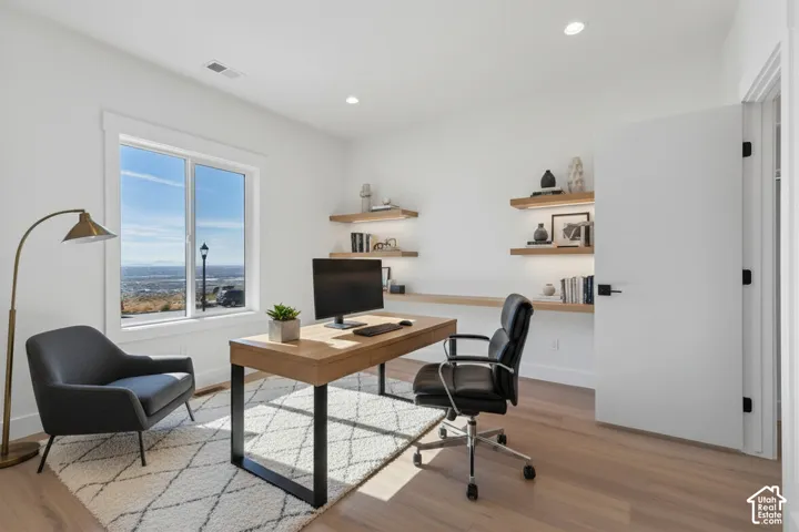 Light wood-finish flooring, built-in open shelving, recessed lighting, white walls, and a white interior door with black hardware