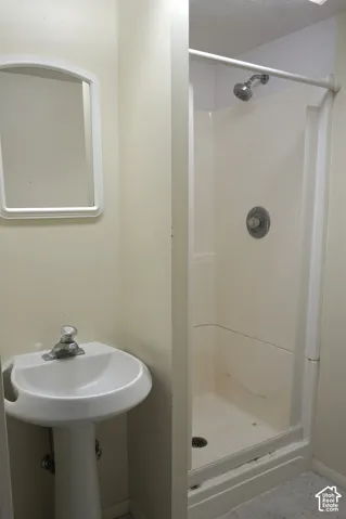 Pedestal sink with chrome faucet, wall-mounted mirror, and a shower stall with a single-handle control