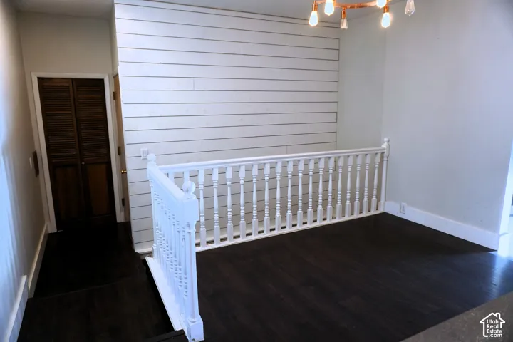 Dark wood-finish flooring, white shiplap accent wall, white baluster railing, and a modern ceiling fixture